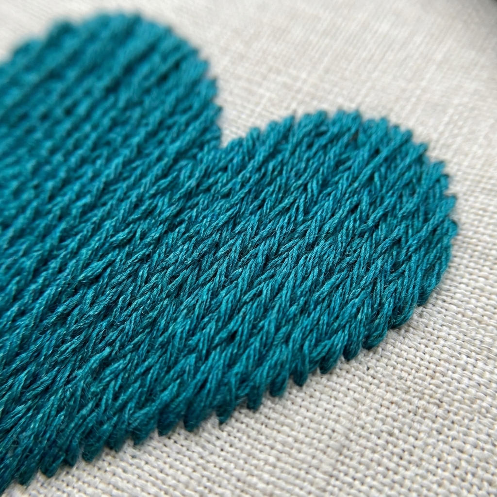 A close-up photograph of split stitch fill inside a heart shape on linen, showing closely packed rows with a soft matte texture